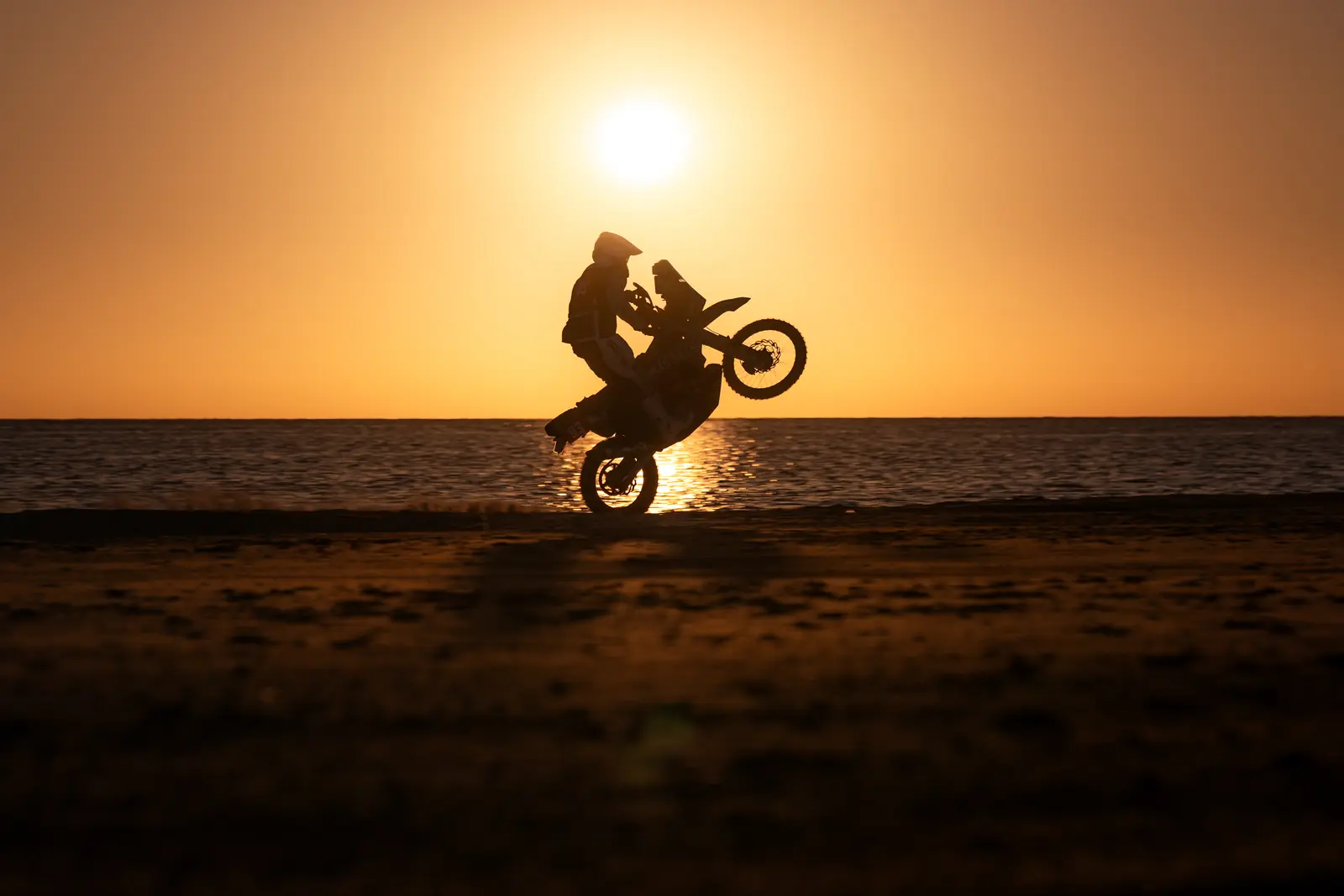 Un pilota in impennata controluce sulla spiaggia al tramonto, Dakar 2026